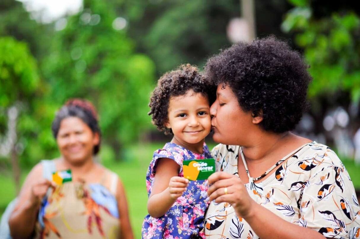 Imagem mãe beijando criança que segura o cartão do programa