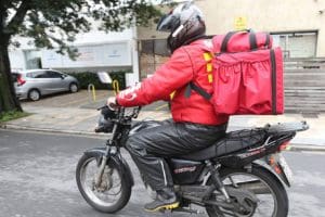 Imagem motociclista em cima da moto com blusa e bag vermela
