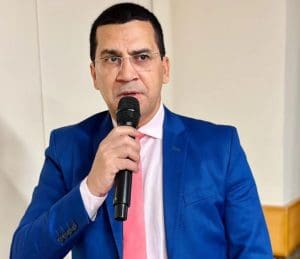 Imagem Hélio Lopes com microfone na mão, ele está com terno azul e gravata cor de rosa