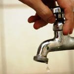 Imagem mão segurando torneira que está pingado gota de água