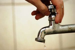 Imagem mão segurando torneira que está pingado gota de água