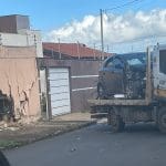 Imagem mostra, à esquerda, um muro amarelo com um buraco grande e irregular, com diversas rachaduras. À direita, um carro HB20 preto com a parte dianteira destruída, em cima de um guincho.