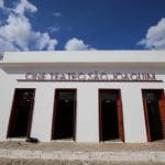 A imagem mostra uma construção vista por baixo. É uma casa térrea, branca. Há quatro portas de madeira, uma do lado da outra, e um letreiro acima delas diz "Cine Teatro São Joaquim".