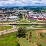 A imagem mostra uma vista aérea do Distrito AgroIndustrial de Anápolis. Uma rodovia corta a imagem horizontalmente. Abaixo, há área verde. Acima, as indústrias.