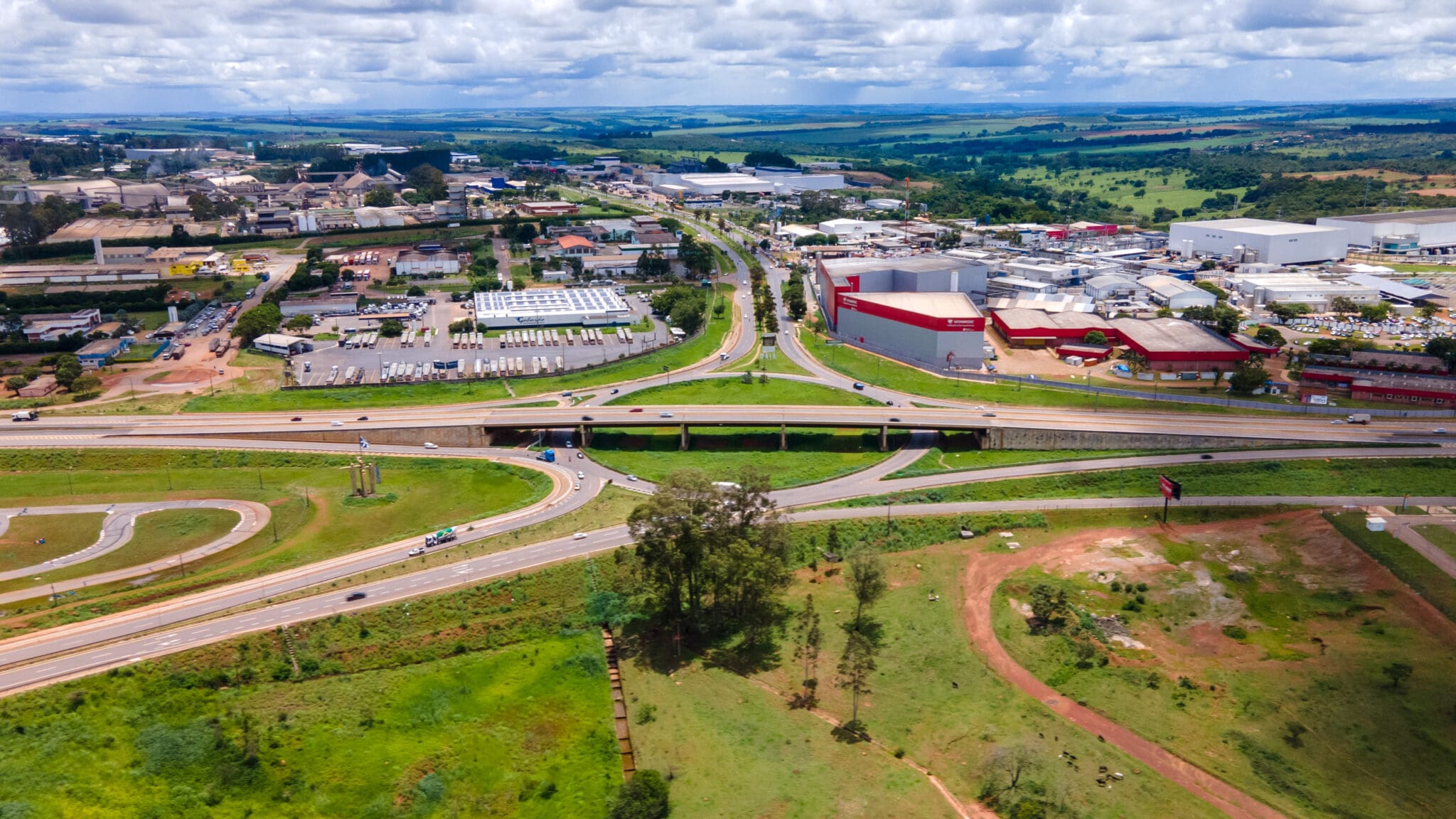 A imagem mostra uma vista aérea do Distrito AgroIndustrial de Anápolis. Uma rodovia corta a imagem horizontalmente. Abaixo, há área verde. Acima, as indústrias.