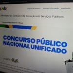 Uma tela de computador é vista de perto. Letras maiúsculas azuis dizem "concurso público nacional unificado". É possível ver o logo do Gov.br, colorido.