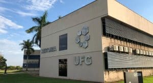 A imagem mostra um prédio bege com letreiros que dizem "Reitoria" e "UFG", além da logo com hexágonos da universidade.