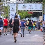 Imagem Corrida de Rua Anápolis. É possível ver as costas de várias pessoas em uma corrida. A chegada está próxima, com um cronômetro que marca 30 minutos.
