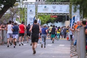 Imagem Corrida de Rua Anápolis. É possível ver as costas de várias pessoas em uma corrida. A chegada está próxima, com um cronômetro que marca 30 minutos.