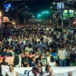 Várias pessoas caminham juntas na rua. Está de noite.