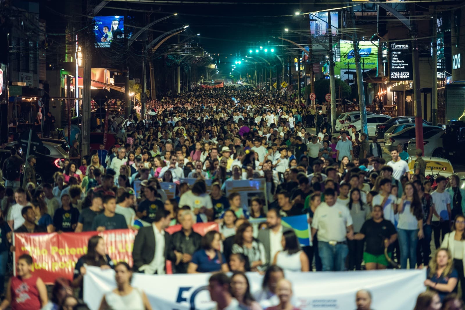 Várias pessoas caminham juntas na rua. Está de noite.