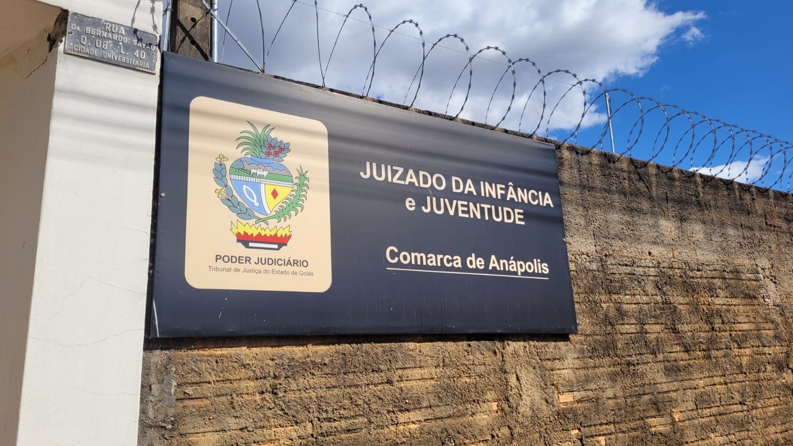 Uma placa em um muro diz: Juizado da infância e juventude, comarca de Anápolis. À esquerda da escrita, um brasão do poder judiciário.