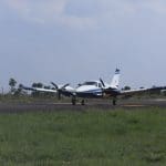 Uma aeronave está parada em uma pista de aterrisagem. Ao redor, há grama baixa.