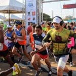Várias pessoas correm na largada de uma corrida. Elas vestem roupas esportivas.