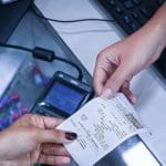 Uma mão passa uma nota fiscal a outra. Não é possível ver de quem são as mãos.