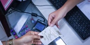 Uma mão passa uma nota fiscal a outra. Não é possível ver de quem são as mãos.