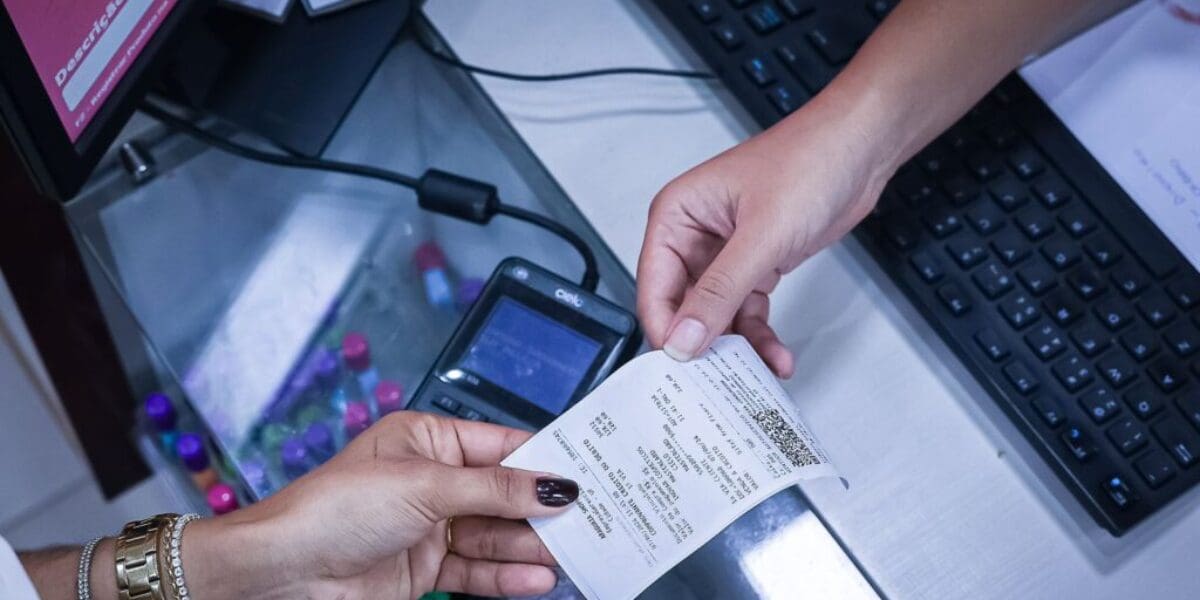 Uma mão passa uma nota fiscal a outra. Não é possível ver de quem são as mãos.