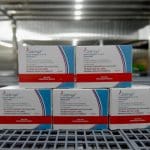 Cinco caixas de imunizante estão empilhados em cima de uma mesa. A caixa diz "Qdenga".