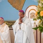 O bispo Dom Dilmo tem os olhos fechados e as mãos juntas em um momento de oração. Ele está dentro da igreja e realiza uma missa. Há outro homem ao seu lado.