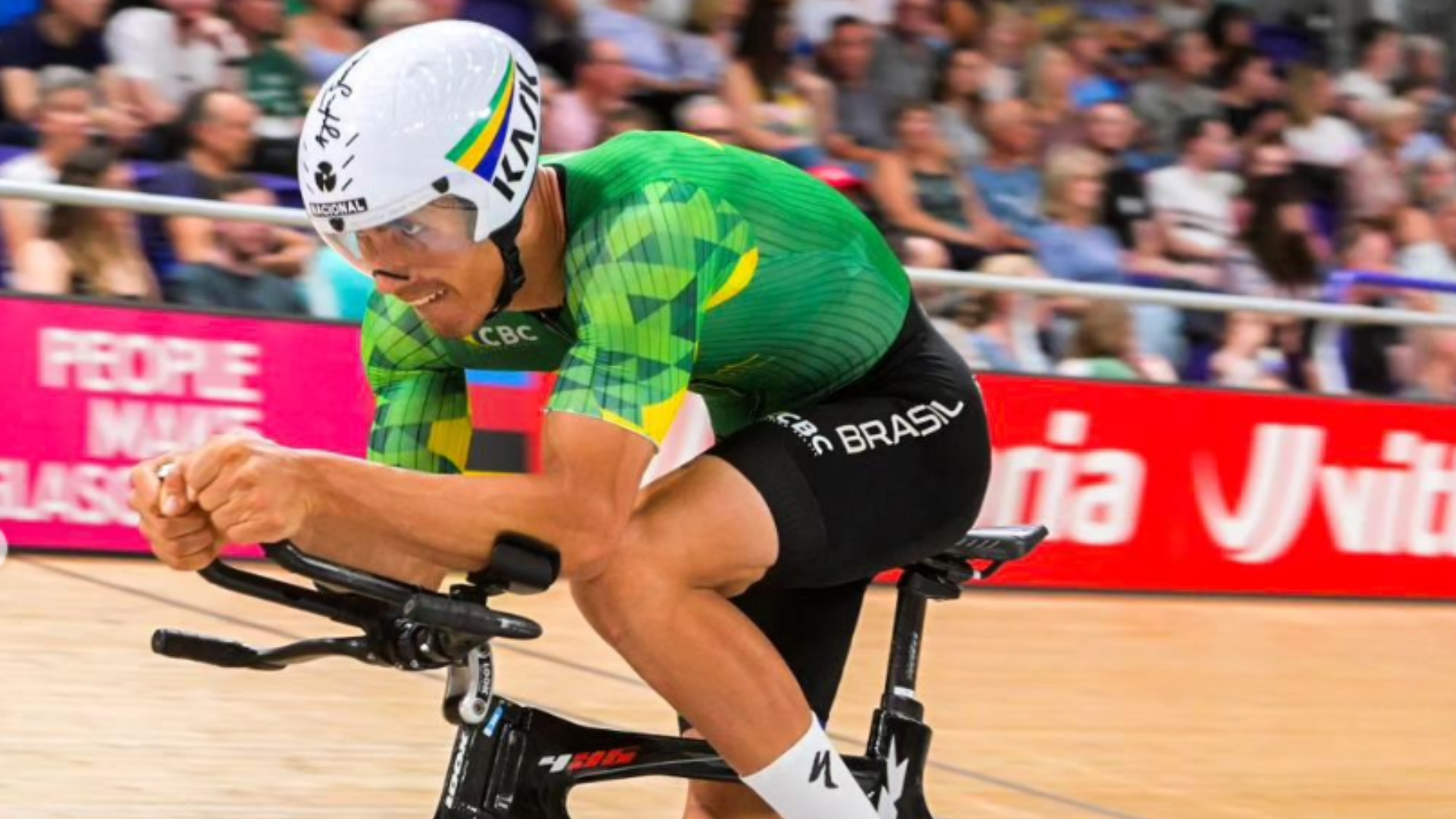 O ciclista Carlos Alberto pedala em uma competição. Ao fundo, a plateia desfocada.