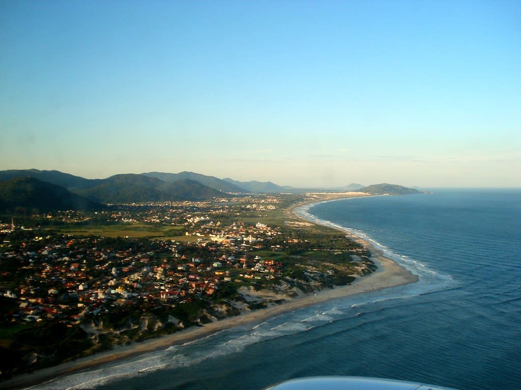 Florianópolis é vista de cima, mostrando a orla com vários prédios e a paisagem ao fundo.