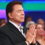 Silvio Santos está com os olhos fechados e as mãos juntas durante um de seus programas no SBT.