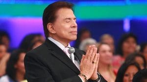 Silvio Santos está com os olhos fechados e as mãos juntas durante um de seus programas no SBT.