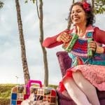 Alicce Oliveira está sentada em uma poltrona enquanto toca uma sanfona ao ar livre.