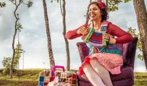 Alicce Oliveira está sentada em uma poltrona enquanto toca uma sanfona ao ar livre.