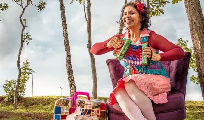 Alicce Oliveira está sentada em uma poltrona enquanto toca uma sanfona ao ar livre.