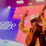 Um violeiro toca em frente ao telão que diz "Circuito Anapolino de Música".