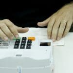 Mesário confere título eleitoral na máquina de biometria.