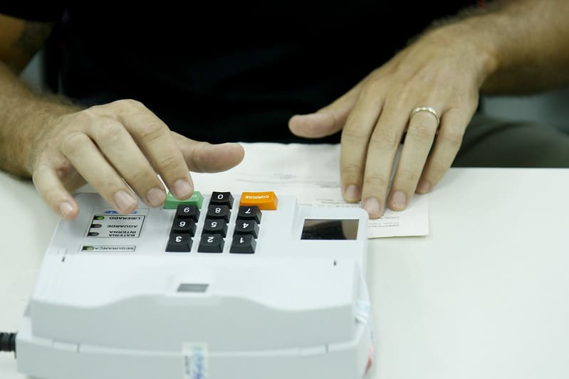 Mesário confere título eleitoral na máquina de biometria.