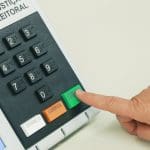 Mão pressiona a tecla de "confirma" na urna eletrônica.