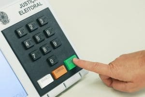 Mão pressiona a tecla de "confirma" na urna eletrônica.