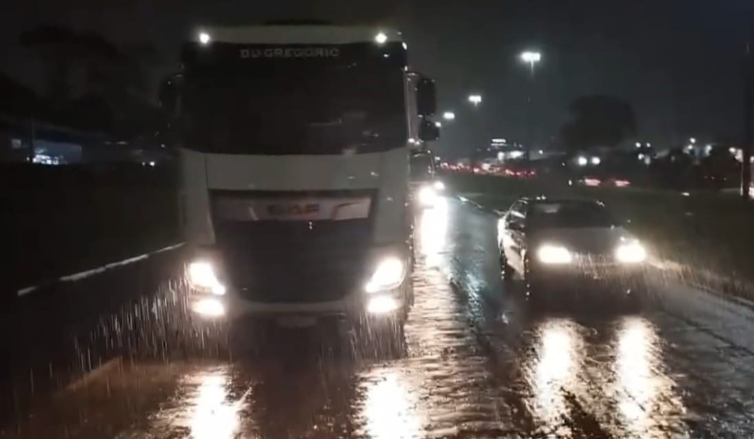 Um caminhão e um carro estão na estrada à noite, enquanto chove.