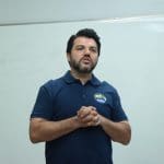 Márcio Corrêa está em pé, enquanto fala com as mãos juntas.