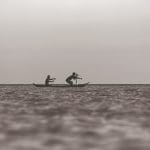 Imagem fotografia de dois homens remando em um barco na aguá