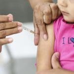 Uma menina pequena recebe uma dose de vacina injetável.