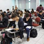 Vários adolescentes estão reunidos em uma sala enquanto realizam uma prova.