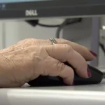 Imagem de uma mão de pessoa mais velha segurando um mouse de computador