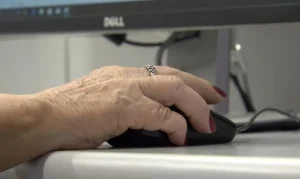 Imagem de uma mão de pessoa mais velha segurando um mouse de computador