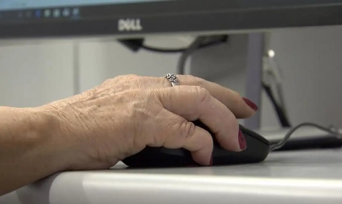 Imagem de uma mão de pessoa mais velha segurando um mouse de computador