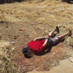 Imagem homem de camisa vermelha algemado e deitado no chão