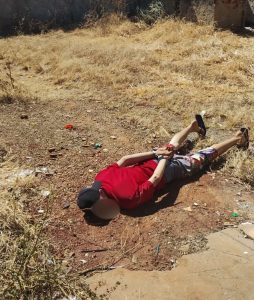 Imagem homem de camisa vermelha algemado e deitado no chão