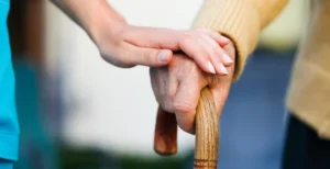 Imagem mão de idoso segurando bengala e uma mão jovem por cima