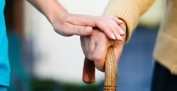 Imagem mão de idoso segurando bengala e uma mão jovem por cima