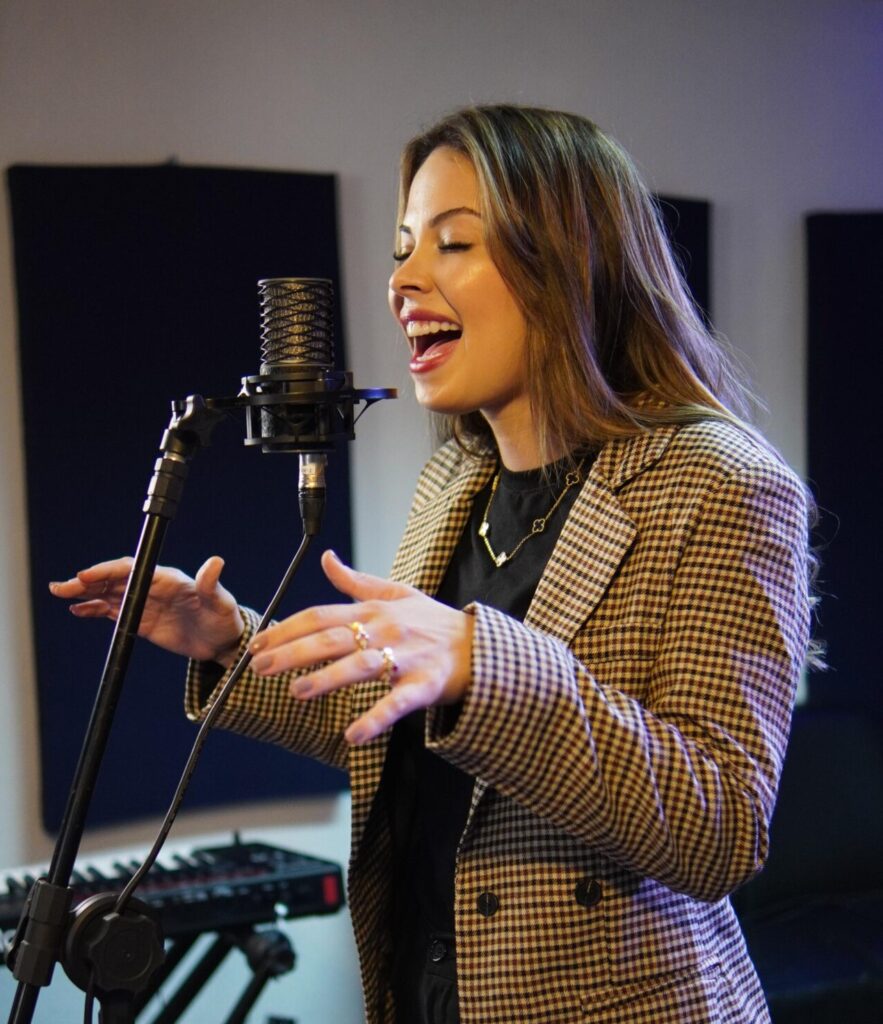 Imagem Bárbara Morgana cantando na frente um microfone no pedestal