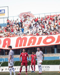 Imagem torcedores no estádio Jonas Duarte, a frente aparecem jogadores da Anapolina e do Tupy de Jussara