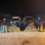 Imagem policiais militares e da PRF segurando armas ao lado de 200kg de drogas apreendidas
